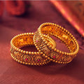 Two gold bangles with intricate designs on a red fabric background