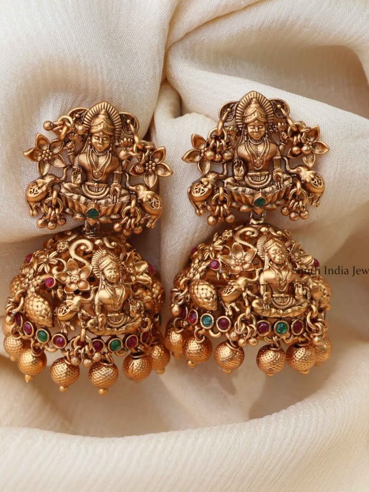 Gold earrings with intricate designs on a beige fabric background