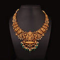 Ornate gold necklace with green stones on a black mannequin