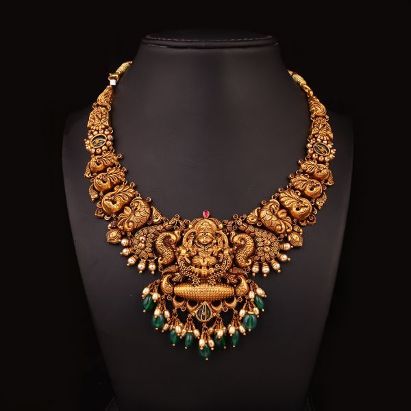 Ornate gold necklace with green stones on a black mannequin