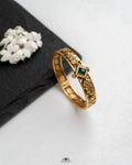 Gold bracelet with a green gemstone on a white surface with black fabric