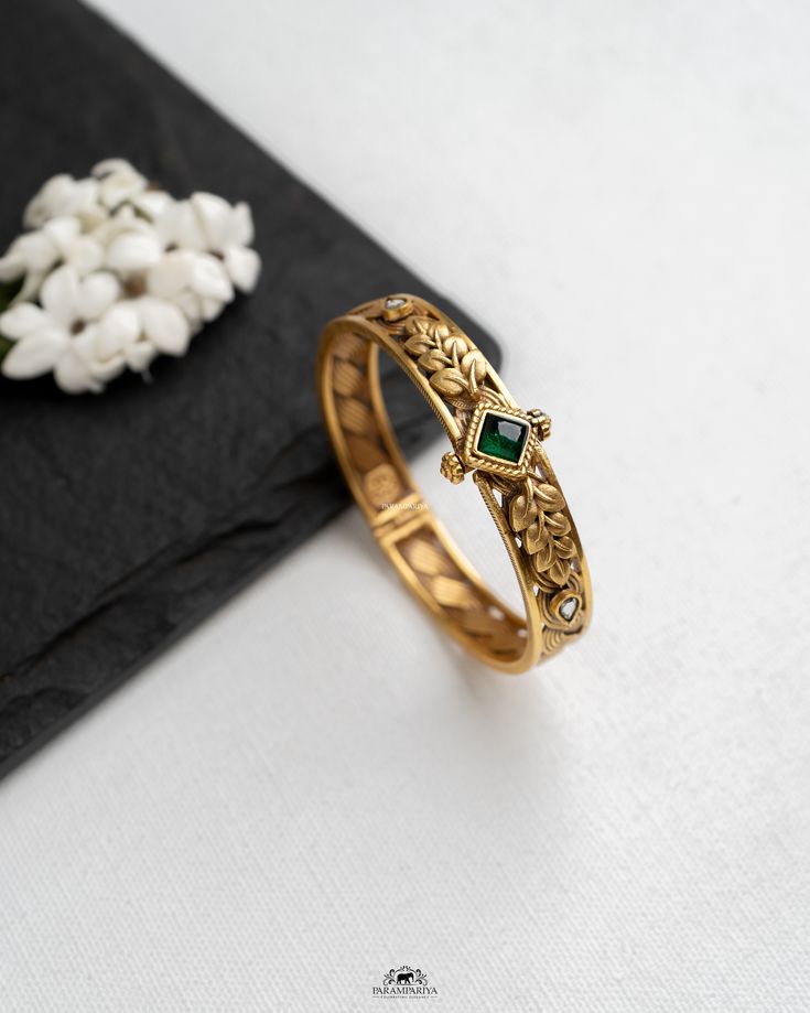 Gold bracelet with a green gemstone on a white surface with black fabric