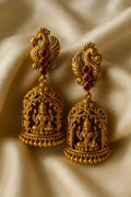 Gold earrings with intricate designs on a beige fabric background