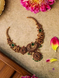 Ornate gold necklace with green stones on a textured surface with flowers