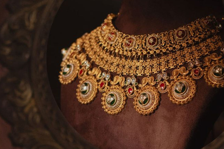 Gold necklace with red stones on a dark background, Umiya Jewellers logo visible