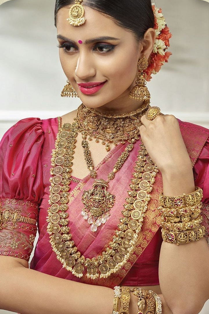 Woman wearing traditional gold jewelry and a pink saree with a white background