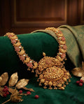 Ornate gold necklace on a green fabric background with leaves and berries.