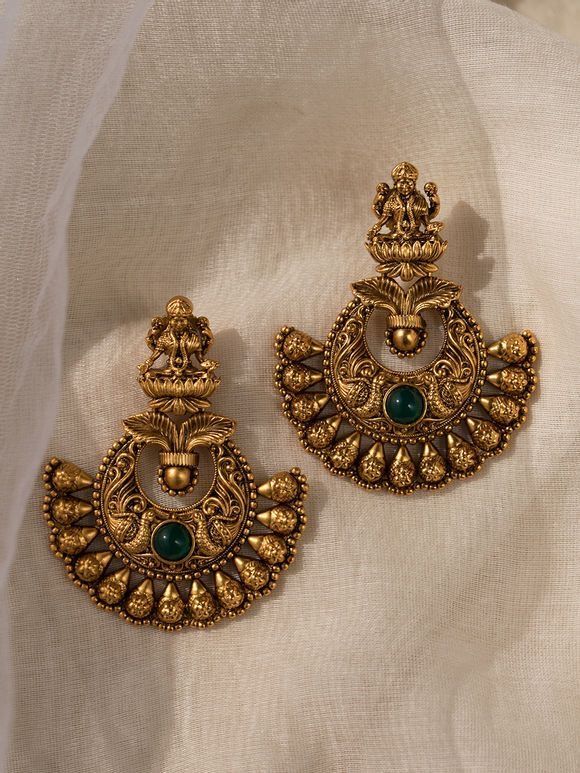 Ornate gold earrings with green gemstones on a sheer fabric background
